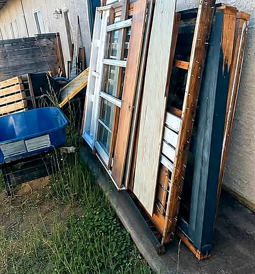 Old doors, window frames and scrap wood stacked along a house, photographed before a MickeyMo job