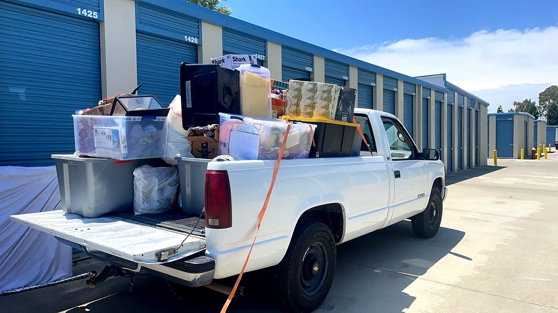 MickeyMo Hauling's white Chevy pickup loaded with bins, boxes and household items at a storage facility